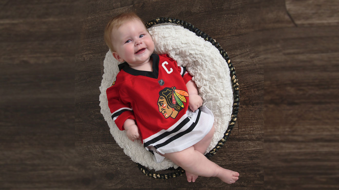 Smiling baby girl wearing a jersey laying in a basket.
