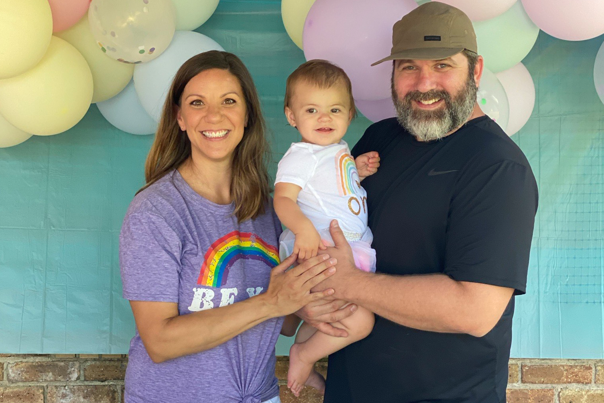 Smiling mom, dad and baby girl in front of birthday balloons