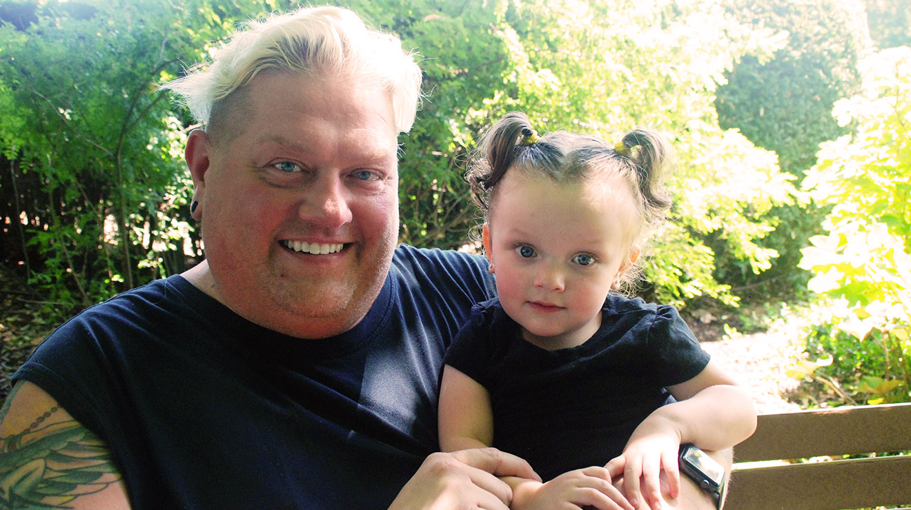 Smiling dad and daughter, both wearing black shirts, sitting outside.