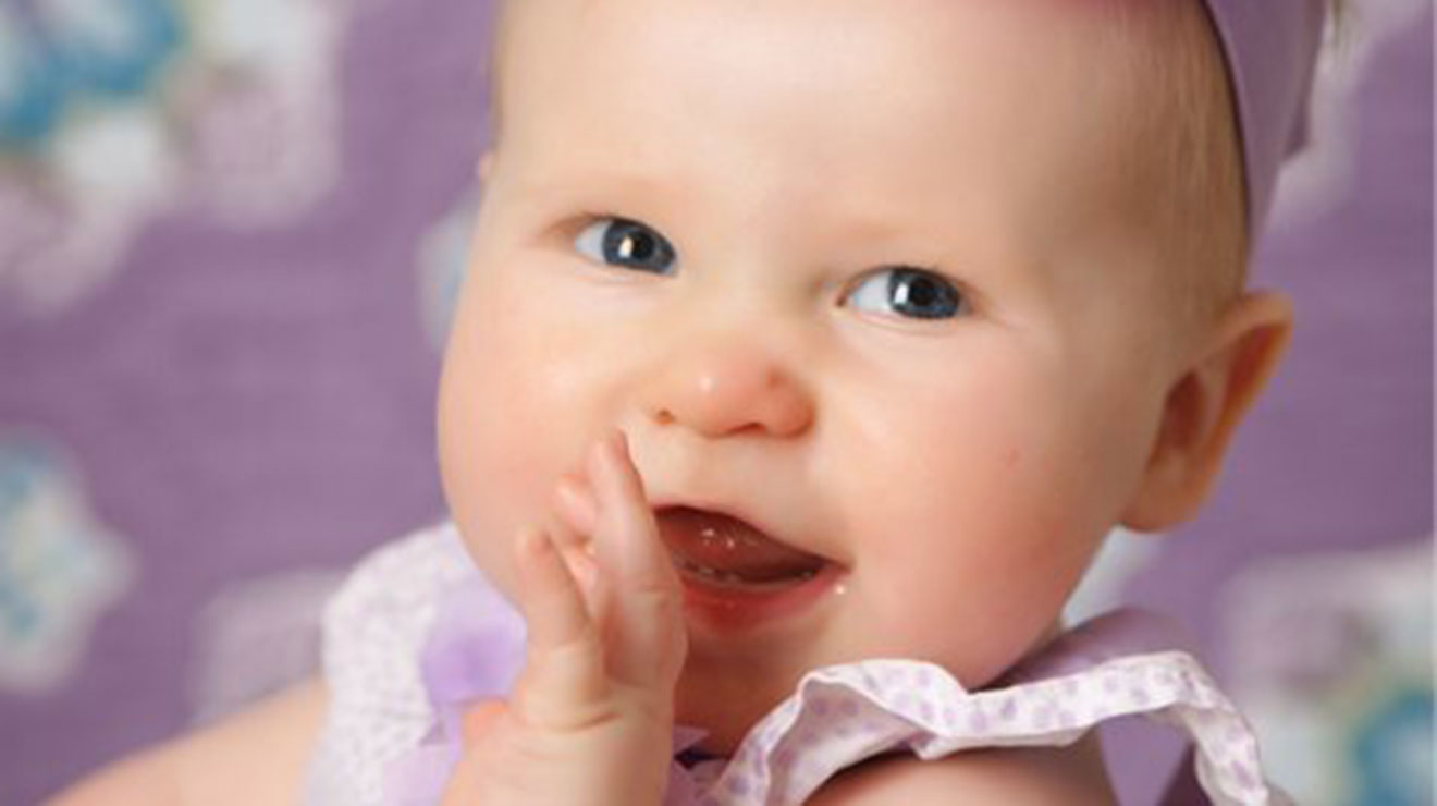 Smiling baby girl wearing a purple outfit and headband.