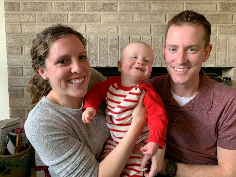 Smiling mom and dad, holding baby boy between them.