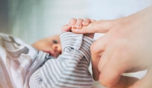 Baby in striped onesie holding mother's finger