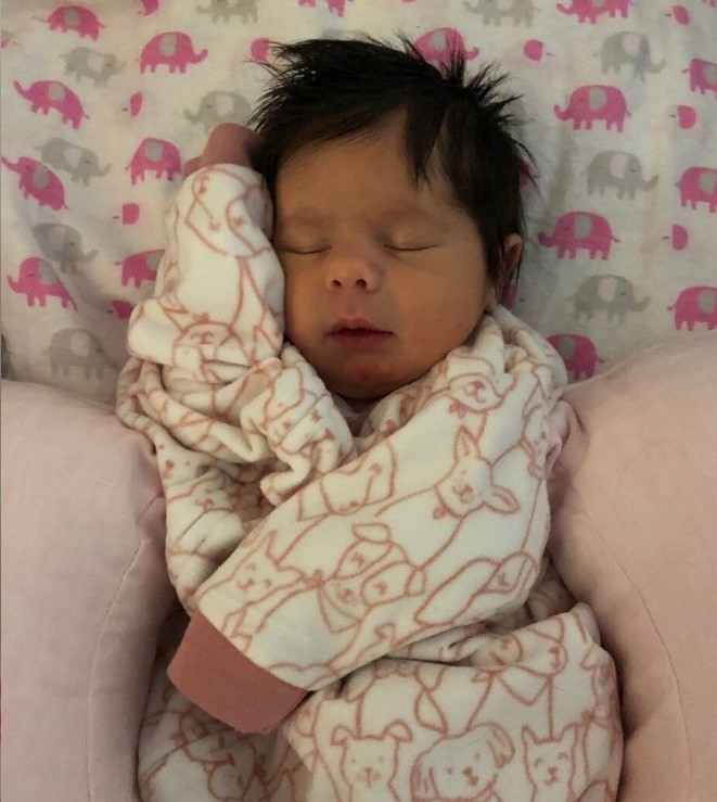 Baby girl wearing white outfit with pink puppies on it, laying on a pink pillow and elephant blanket.
