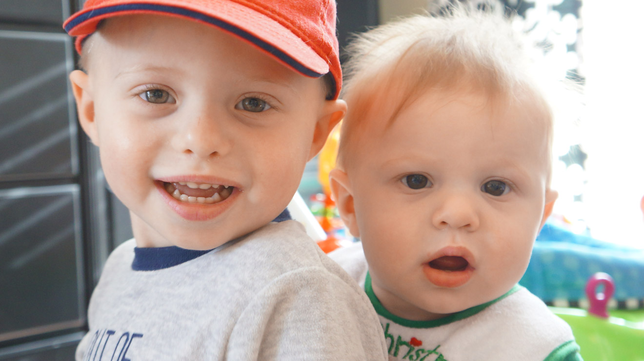 Toddler and newborn brothers looking at the camera.