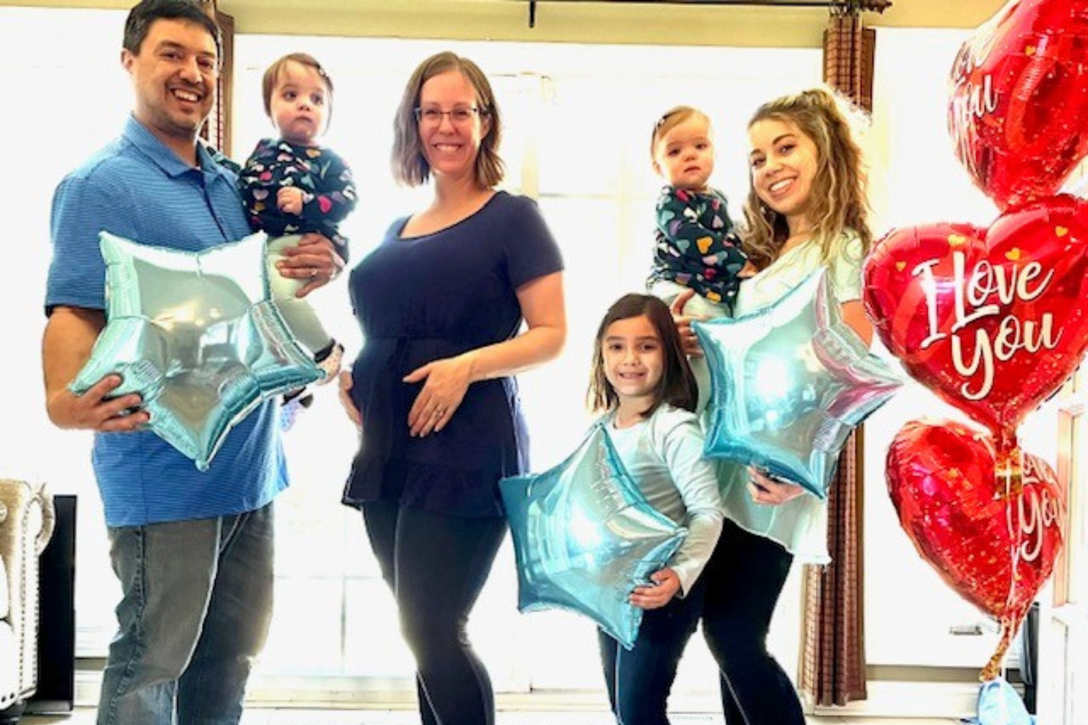 Smiling family with pregnant mom in the center. Star and heart shaped balloons surround the family.