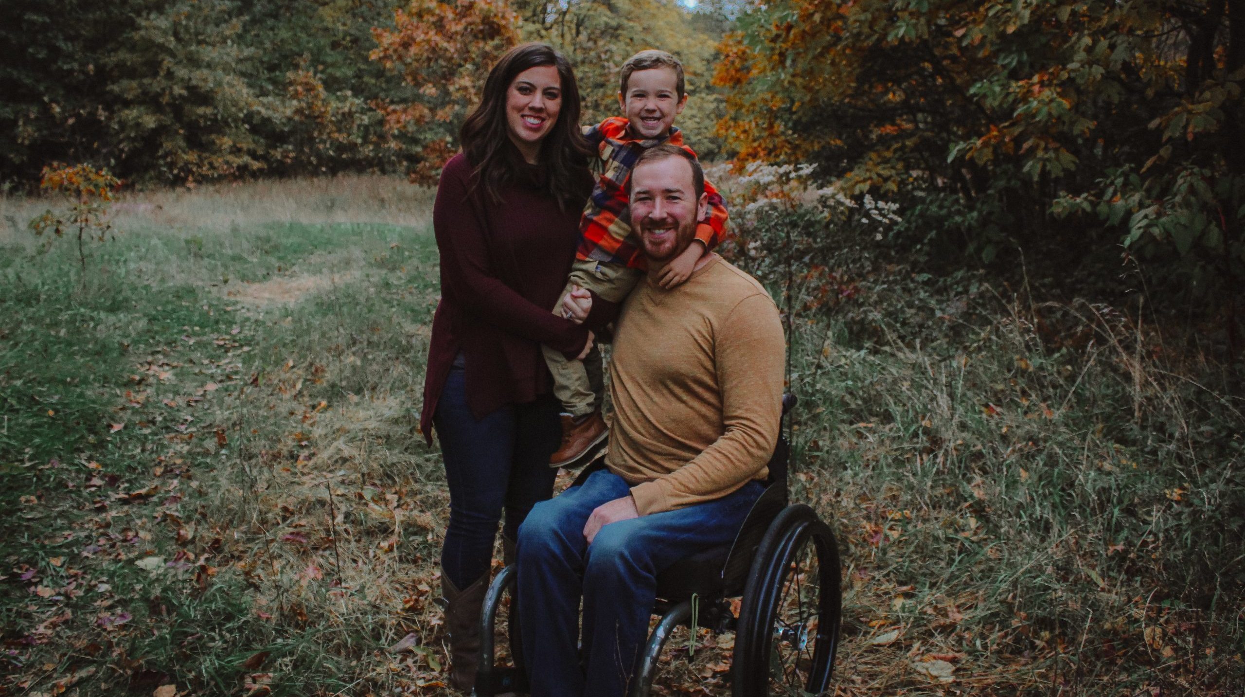 Mom holding toddler son next to dad in wheelchair.