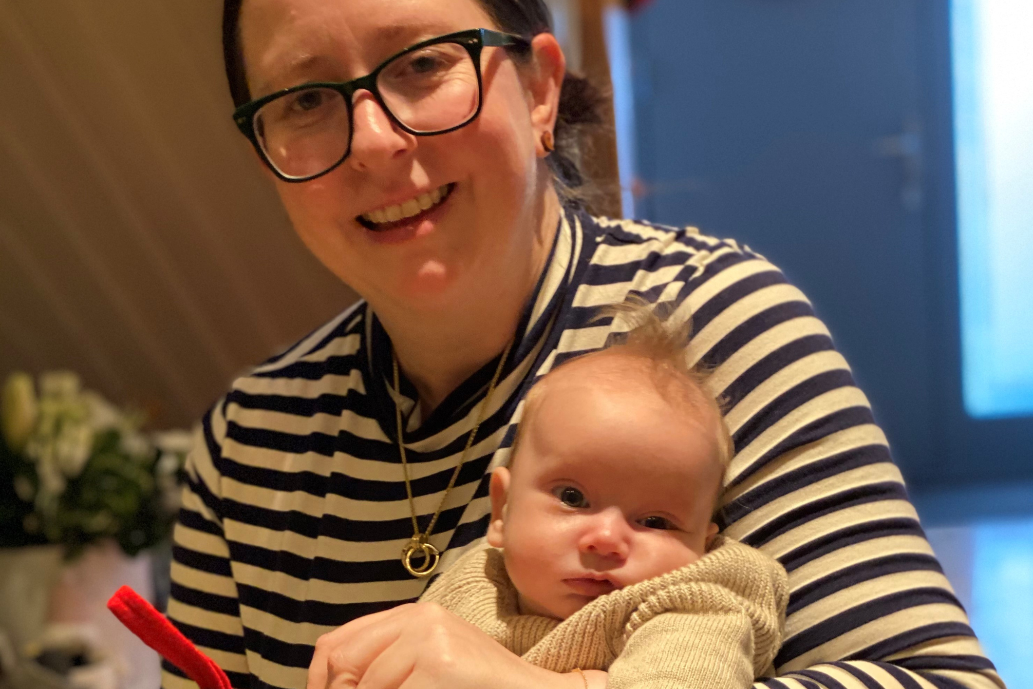 Smiling mom wearing a black and white striped long sleeve top holding her baby wearing a tan sweater.