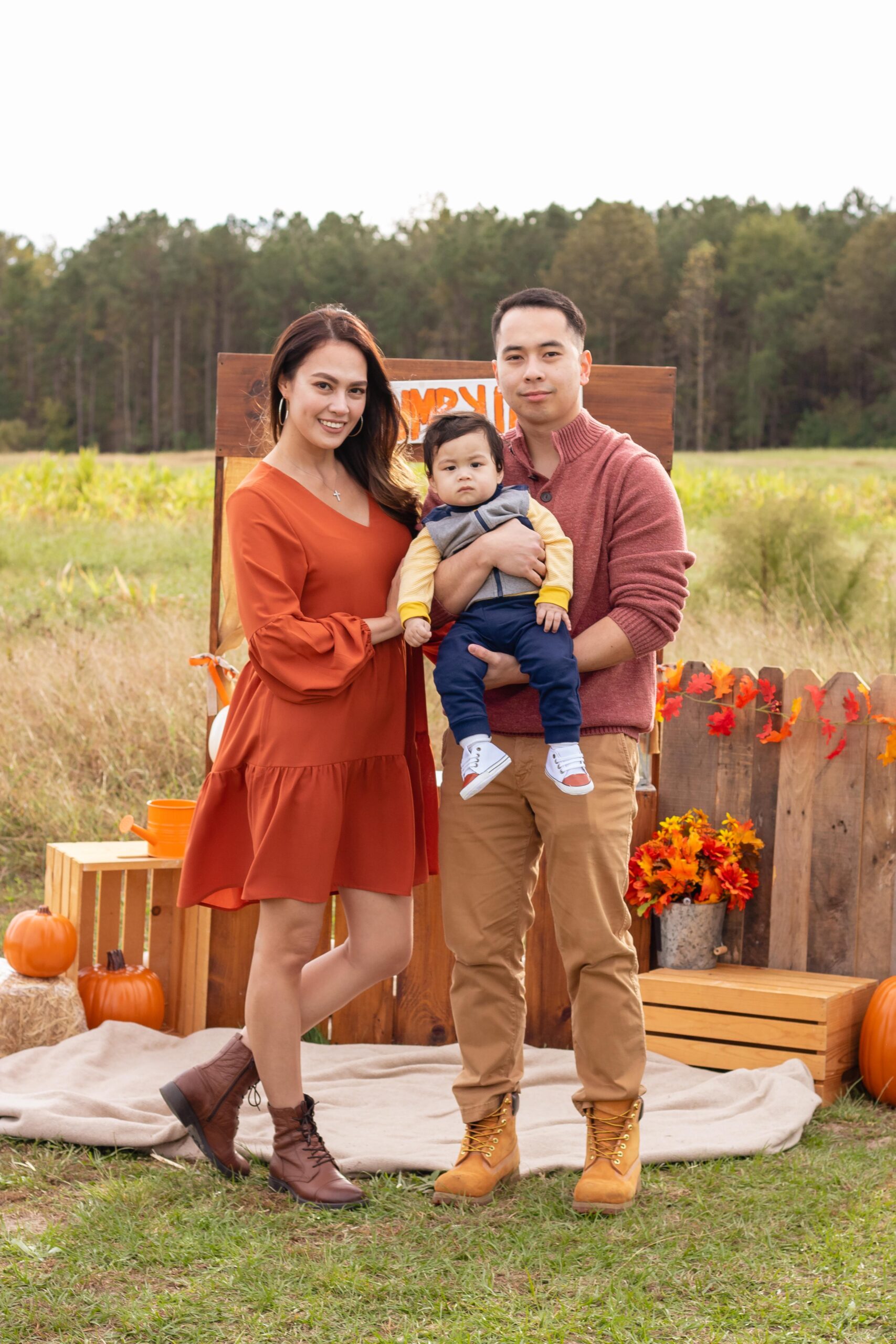 Smiling mom and dad, holding toddler son in pumpkin patch