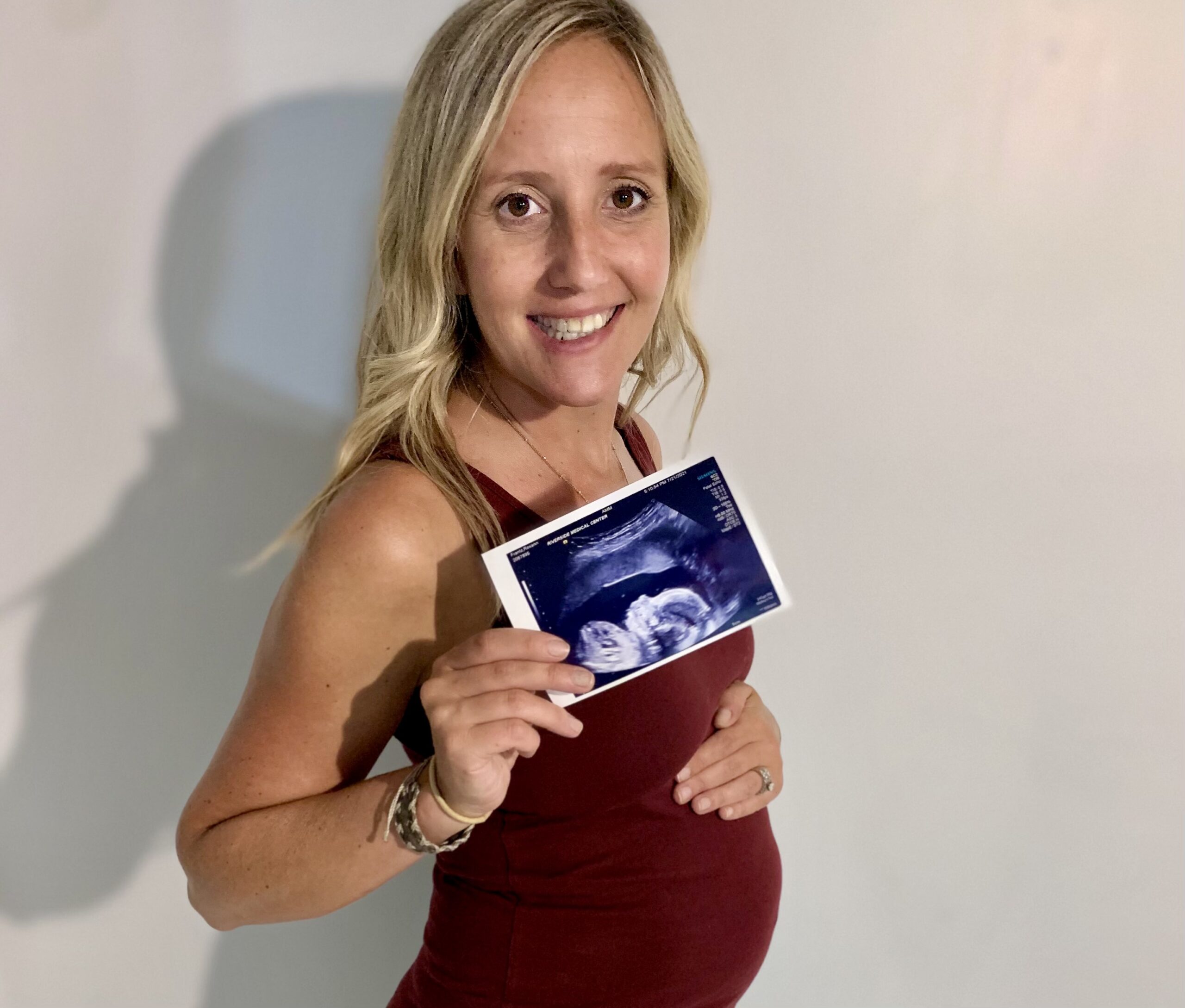 Smiling pregnant mom holding her belly and an ultrasound photo.